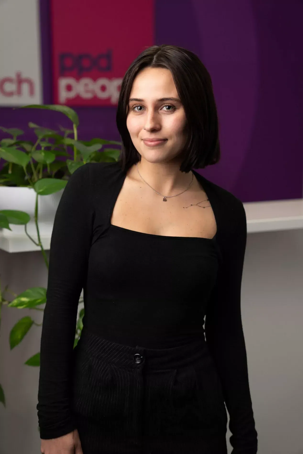 Woman with dark hair, smiling, wearing black top and pants; office setting.