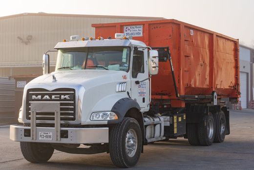 White dump truck with an orange cargo bed parked outdoors near a beige building.