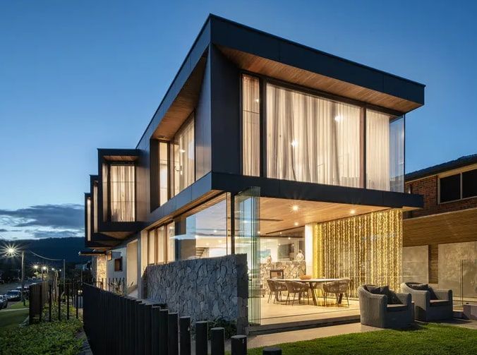 Modern two-story home with dark exterior and large windows, lit up at dusk — Envisage Construction and Design in Mountain, NSW