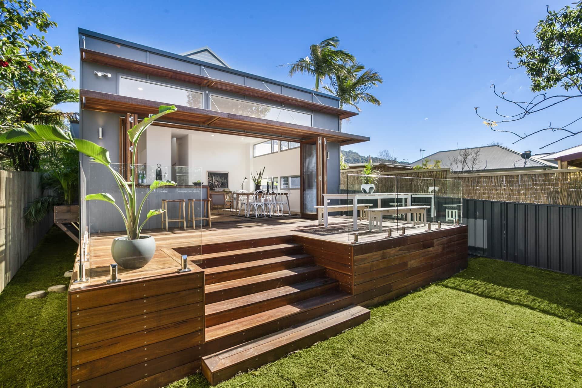 Wooden deck with steps leading to a modern, open-plan extension; green lawn and trees in the backyard — Envisage Construction and Design in Mountain, NSW