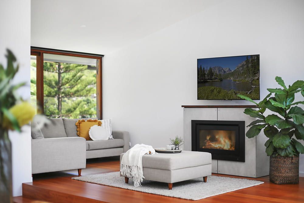 Living Room With Fireplace, Tv, Gray Sofa, and Large Window Overlooking  — Envisage Construction and Design in Koloona Dr, NSW
