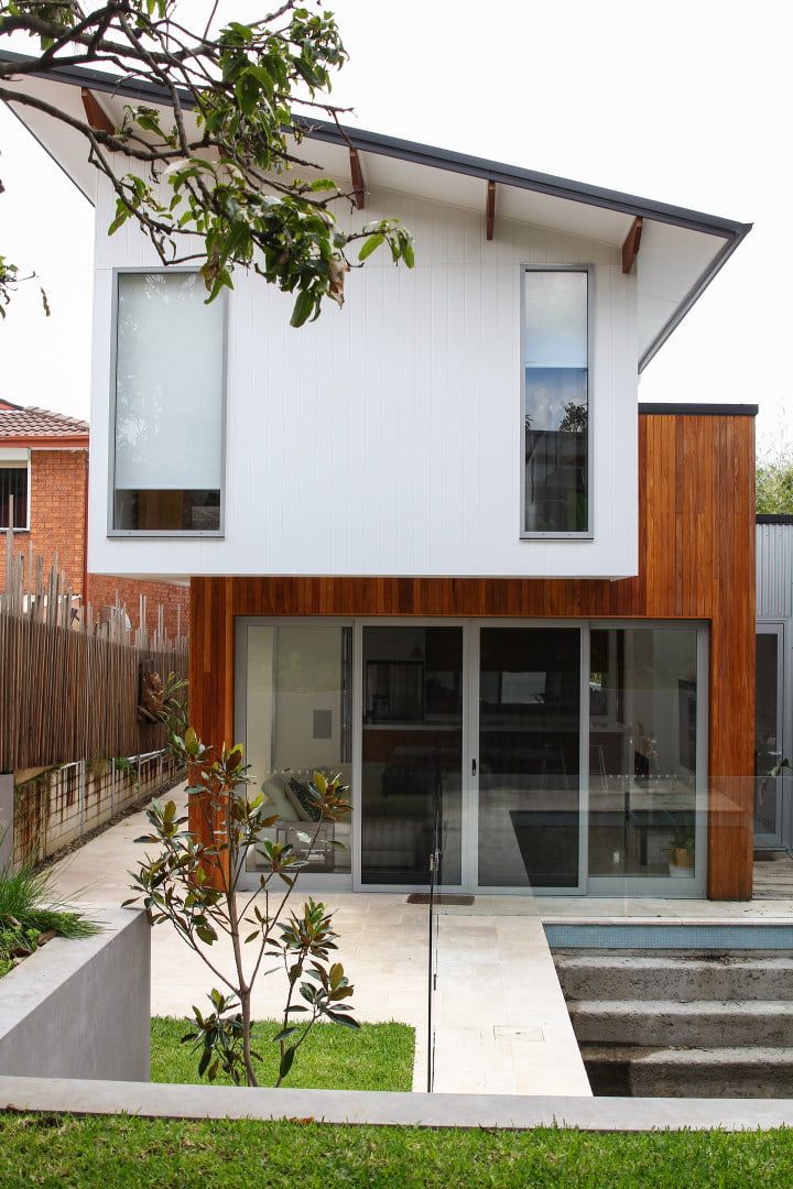 Modern white house with angled roof, wood accents, and glass doors. Concrete path and small garden — Envisage Construction and Design in Mountain, NSW