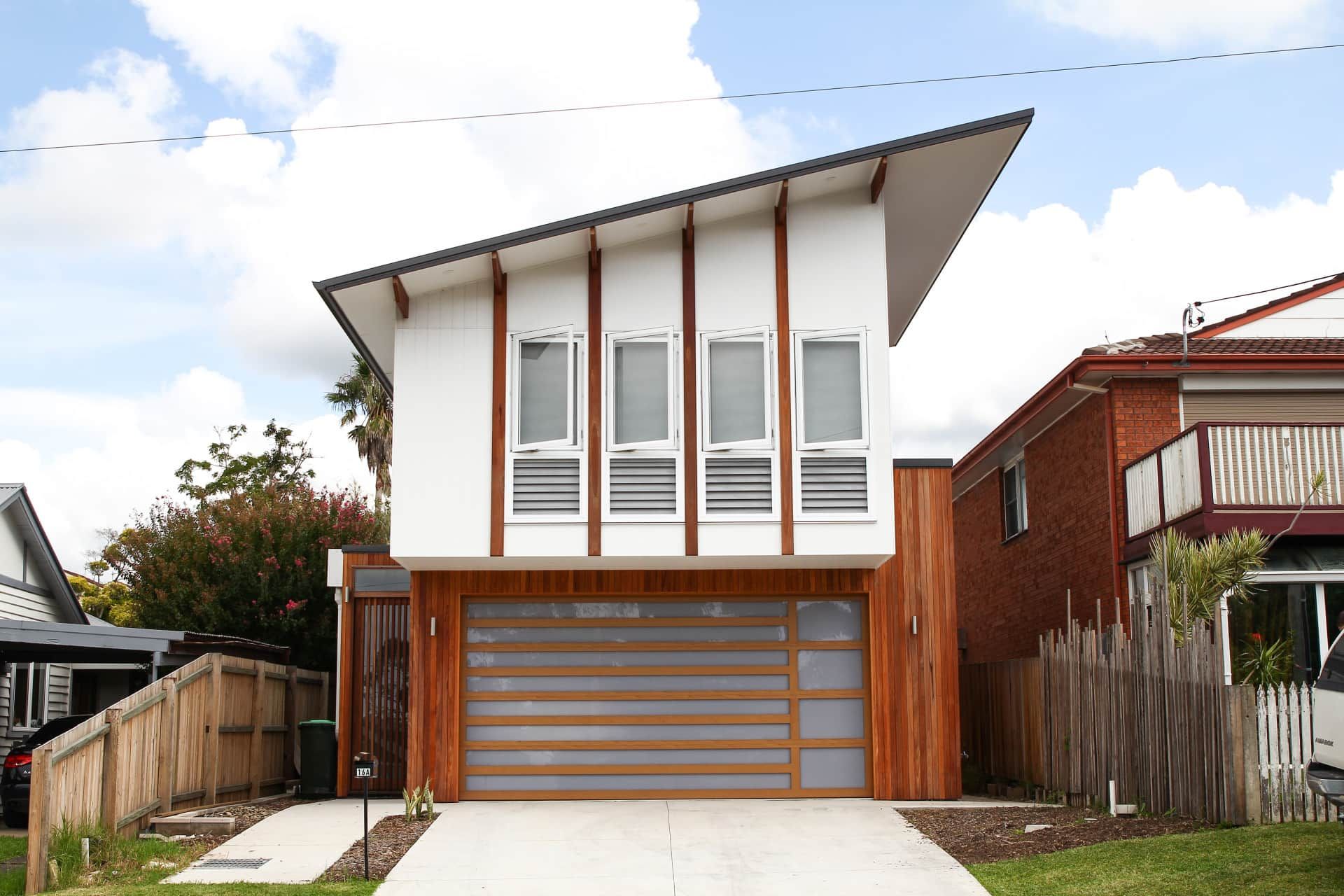 Modern two-story house with a wooden garage door and white walls accented by vertical wooden panels — Envisage Construction and Design in Mountain, NSW