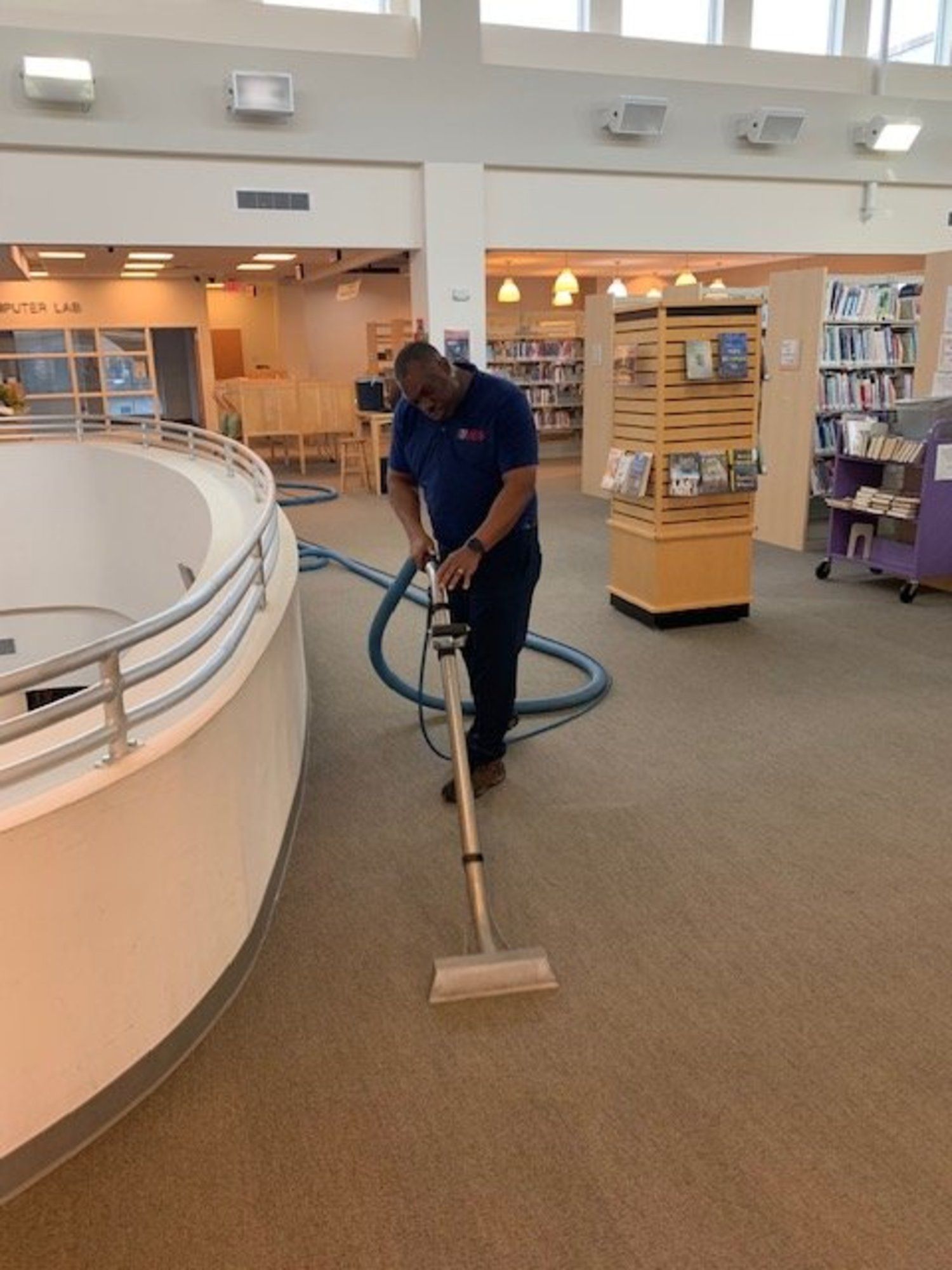 A man is using a vacuum cleaner to clean a carpet in a library.