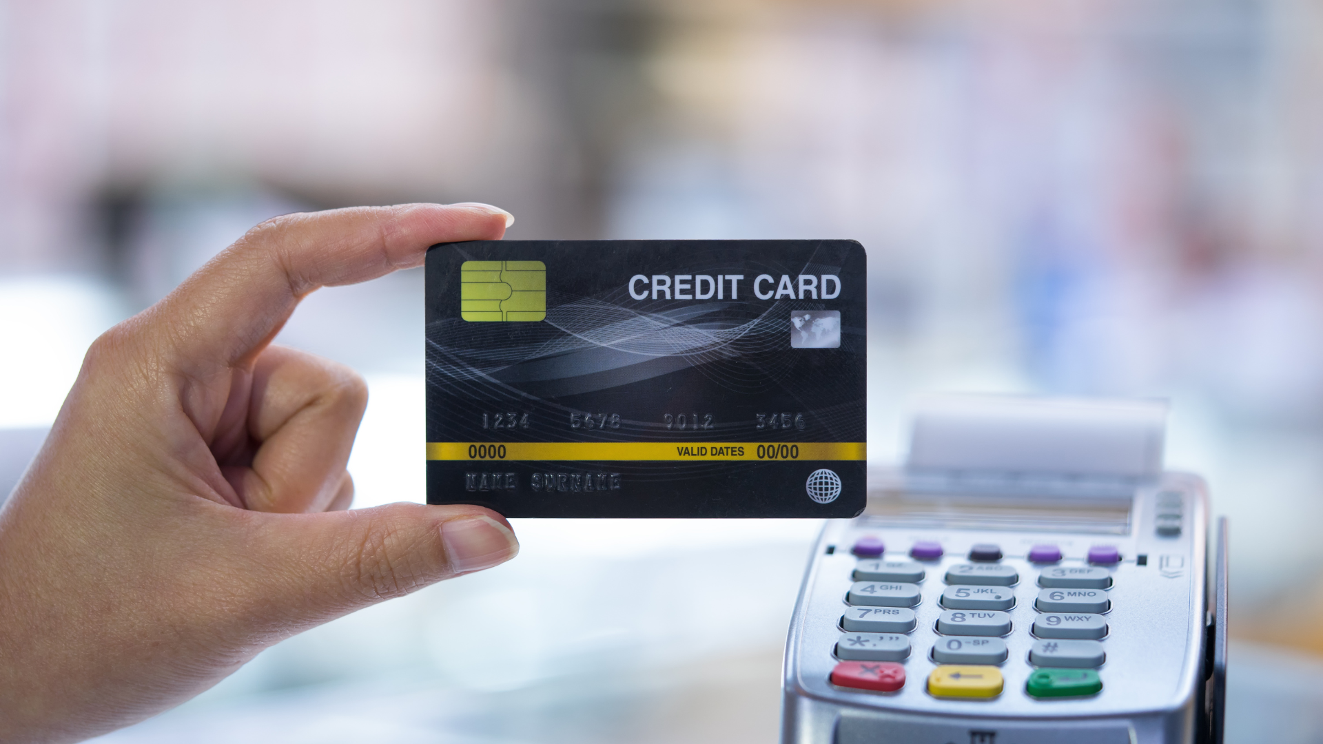 A hand holding a black credit card in front of a payment terminal.