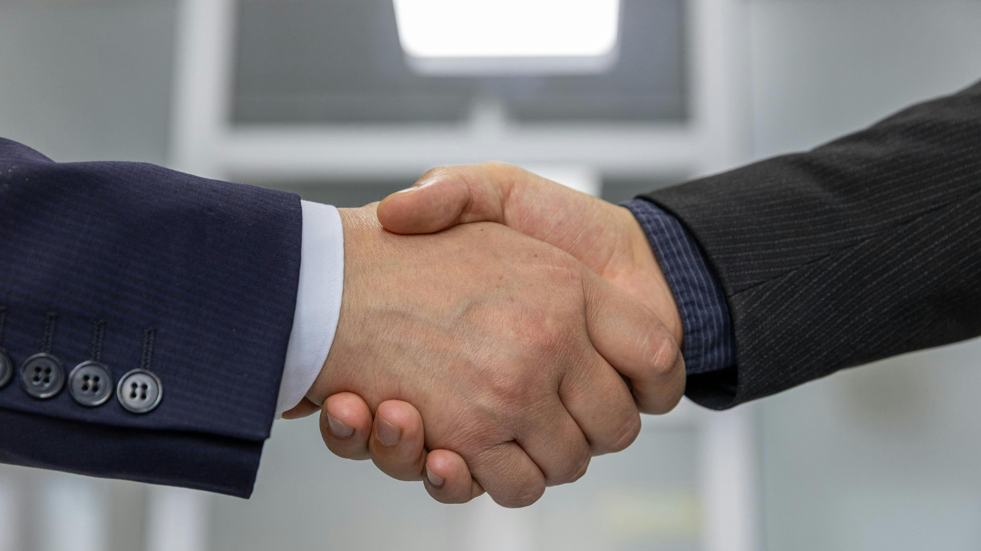 Two people in formal business suits shaking hands in an office setting.