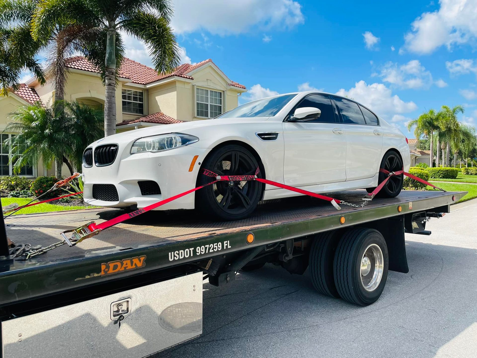 A white bmw is sitting on top of a tow truck.