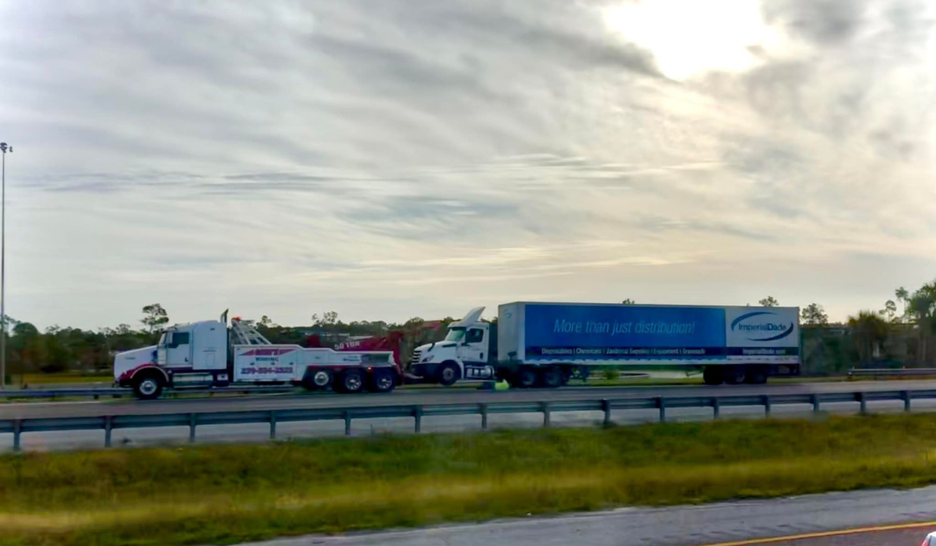 A tow truck is towing a semi truck on a highway.