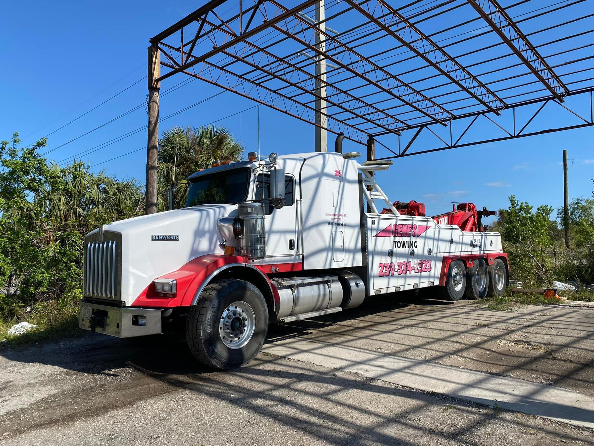 A white and red tow truck is parked under a metal structure.