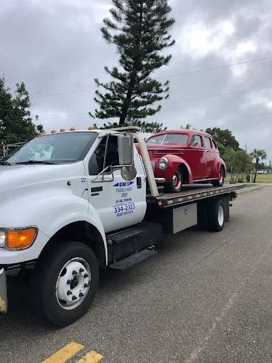 A red classic car is on a white tow truck on a road.