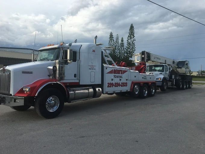 White tow truck hauling a crane truck on a paved road under a cloudy sky.