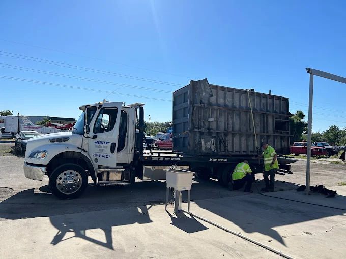 A white truck with a large container, two workers in yellow vests, outdoors.
