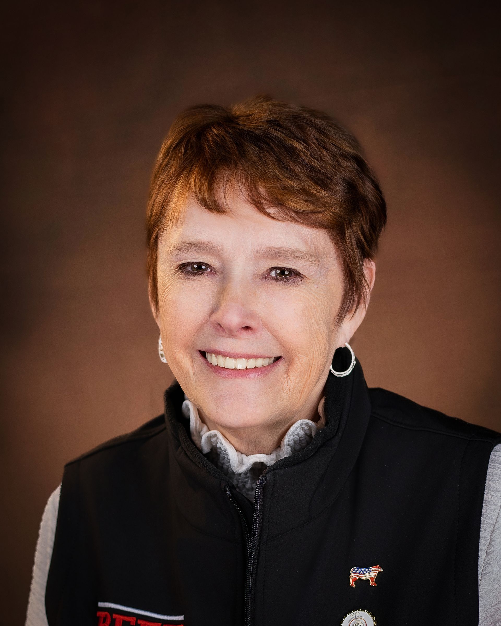 Woman with short auburn hair, wearing black vest, smiling at the camera.