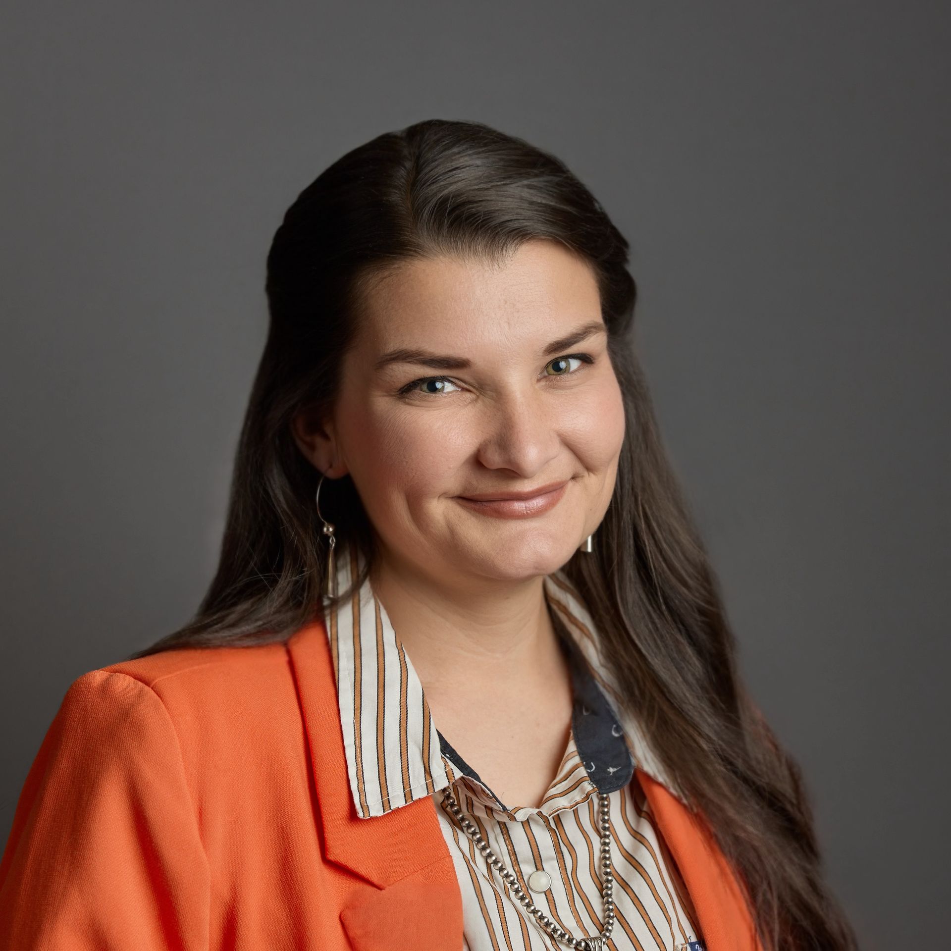 Smiling woman with short gray hair, glasses, and a pink jacket against a brown background.