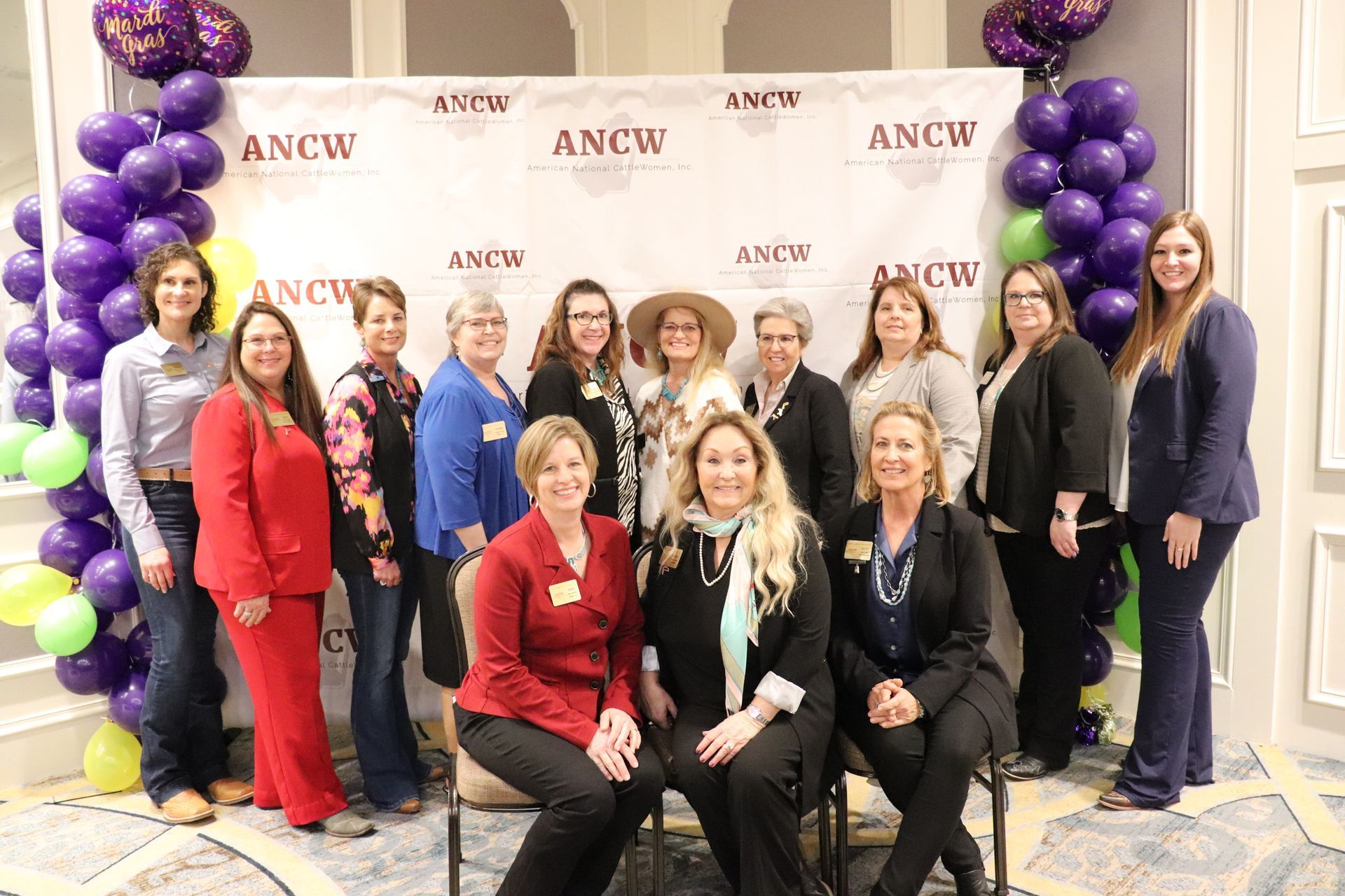 Five women smiling, posing behind illuminated 