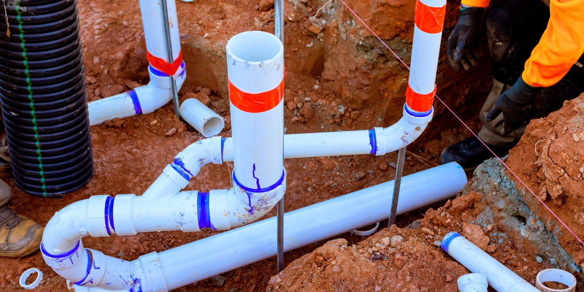 Plumber installing white PVC pipes in a trench. Red and blue markings are visible.