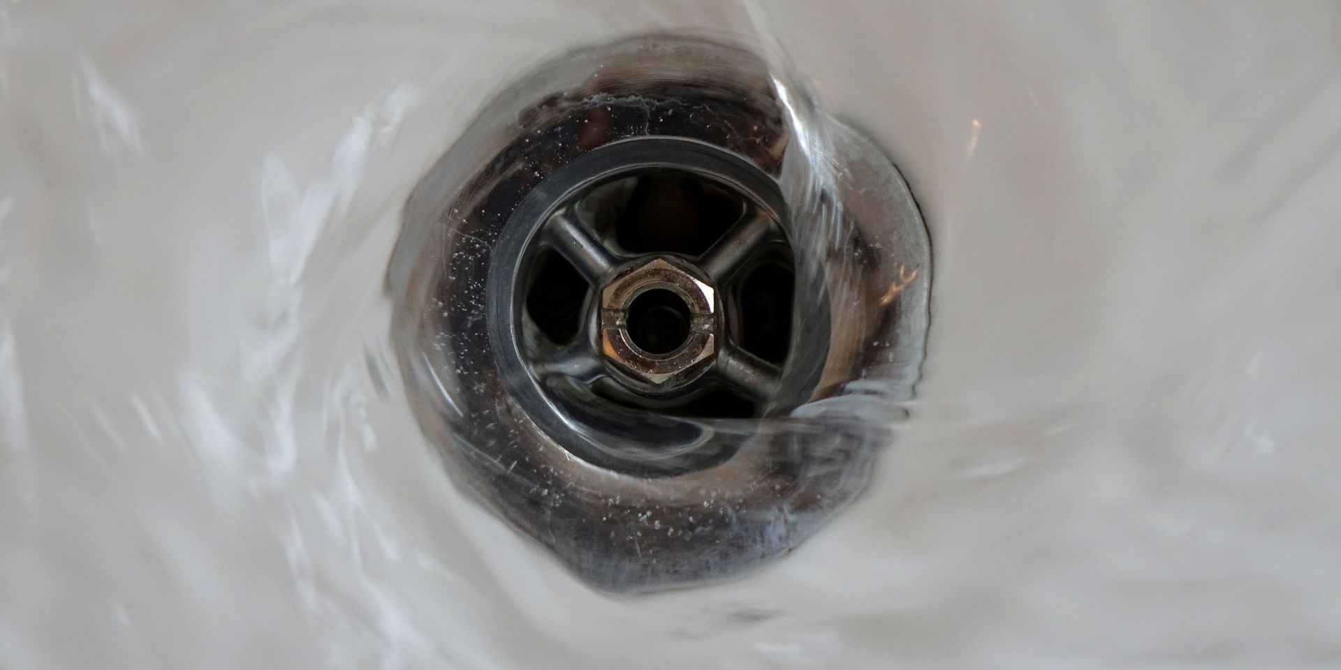 Water flowing down a sink drain; the drain is silver, and the sink is white.