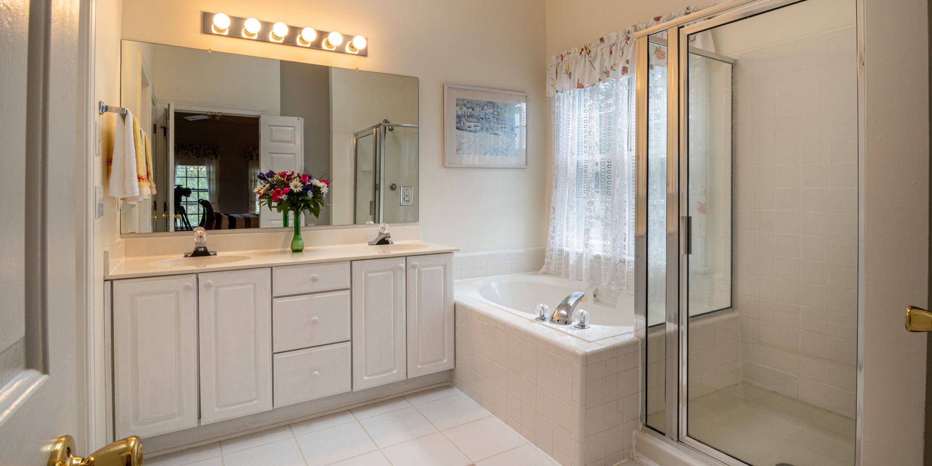 A bright, spacious bathroom with a vanity, tub, and shower. White cabinets and walls give a clean look.