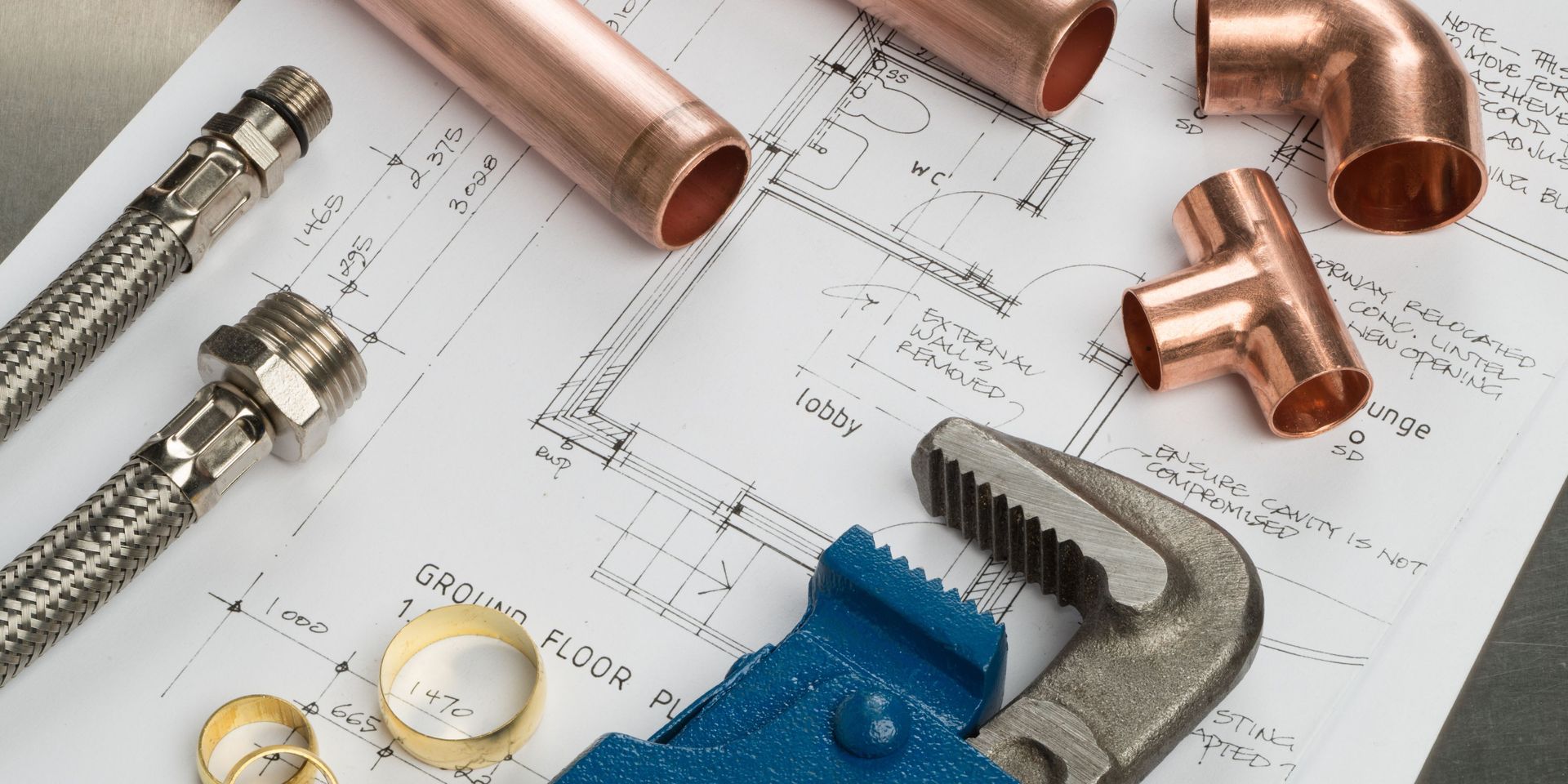 Plumbing tools, copper pipes, and a wrench rest on a blueprint.