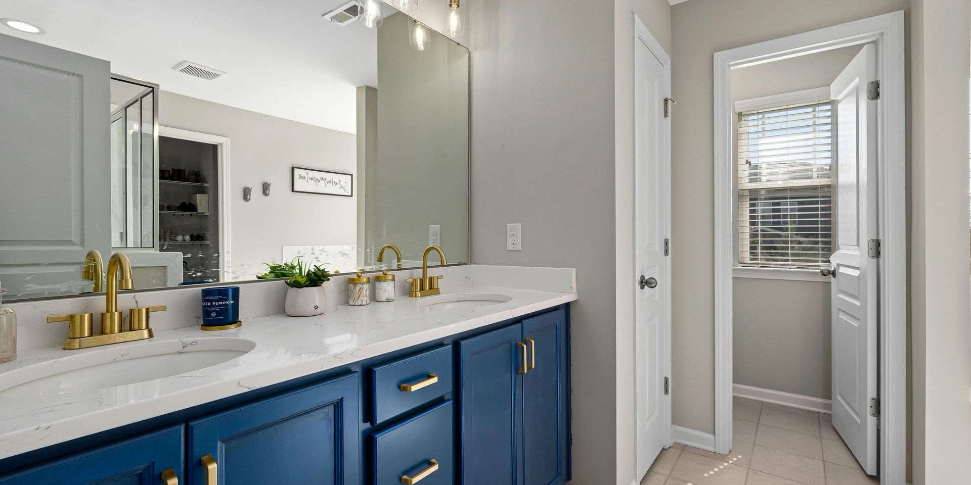 A blue vanity with gold faucets and a mirror in a light-colored bathroom.
