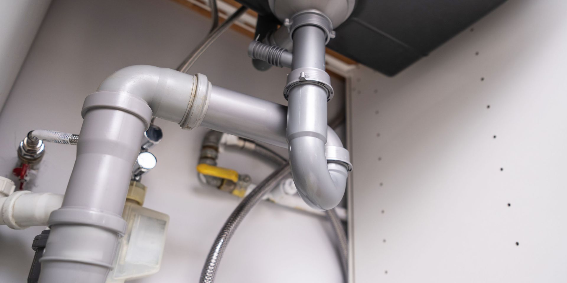 Plumbing pipes under a sink inside a white cabinet.