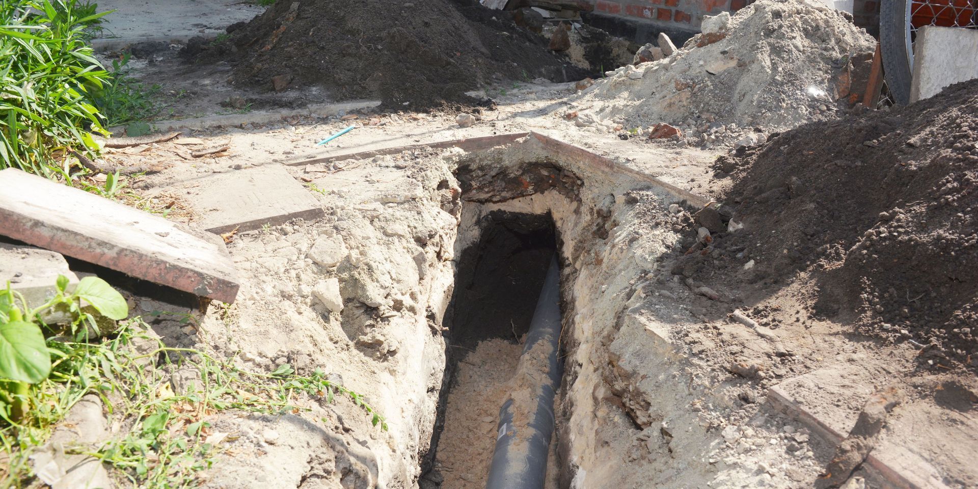 A trench dug in dirt, revealing a dark pipe. Piles of dirt surround the opening.