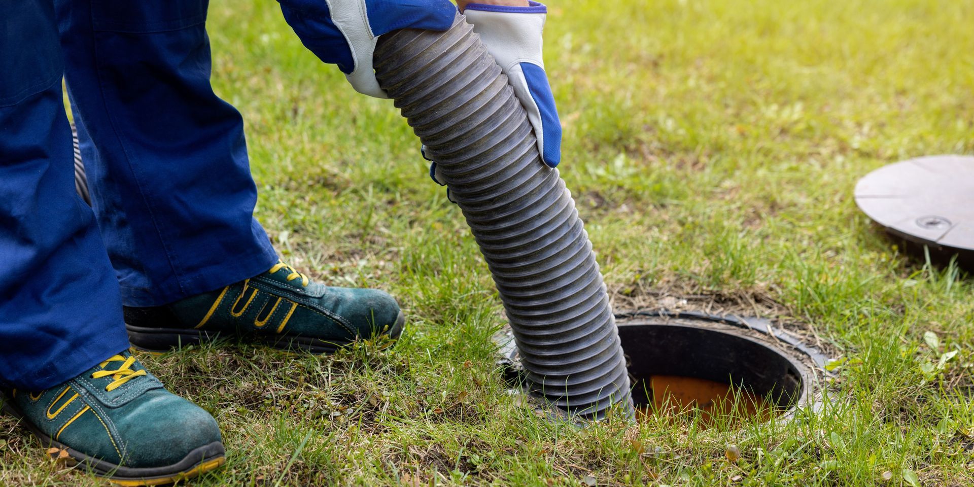 Person pumping sewage from an open septic tank on a grassy lawn.