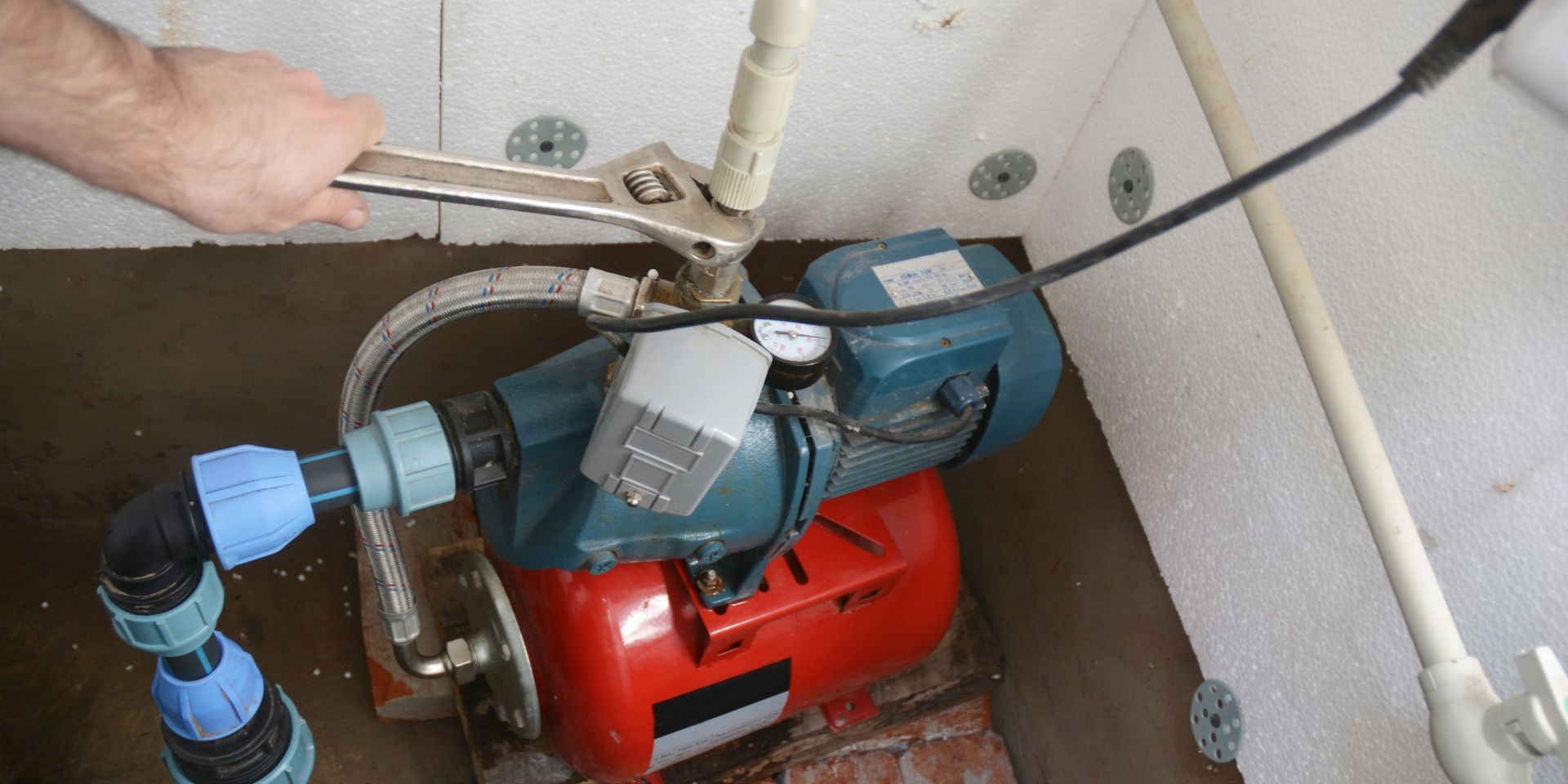 Person using a wrench to tighten a pipe connection on a water pump, indoors.
