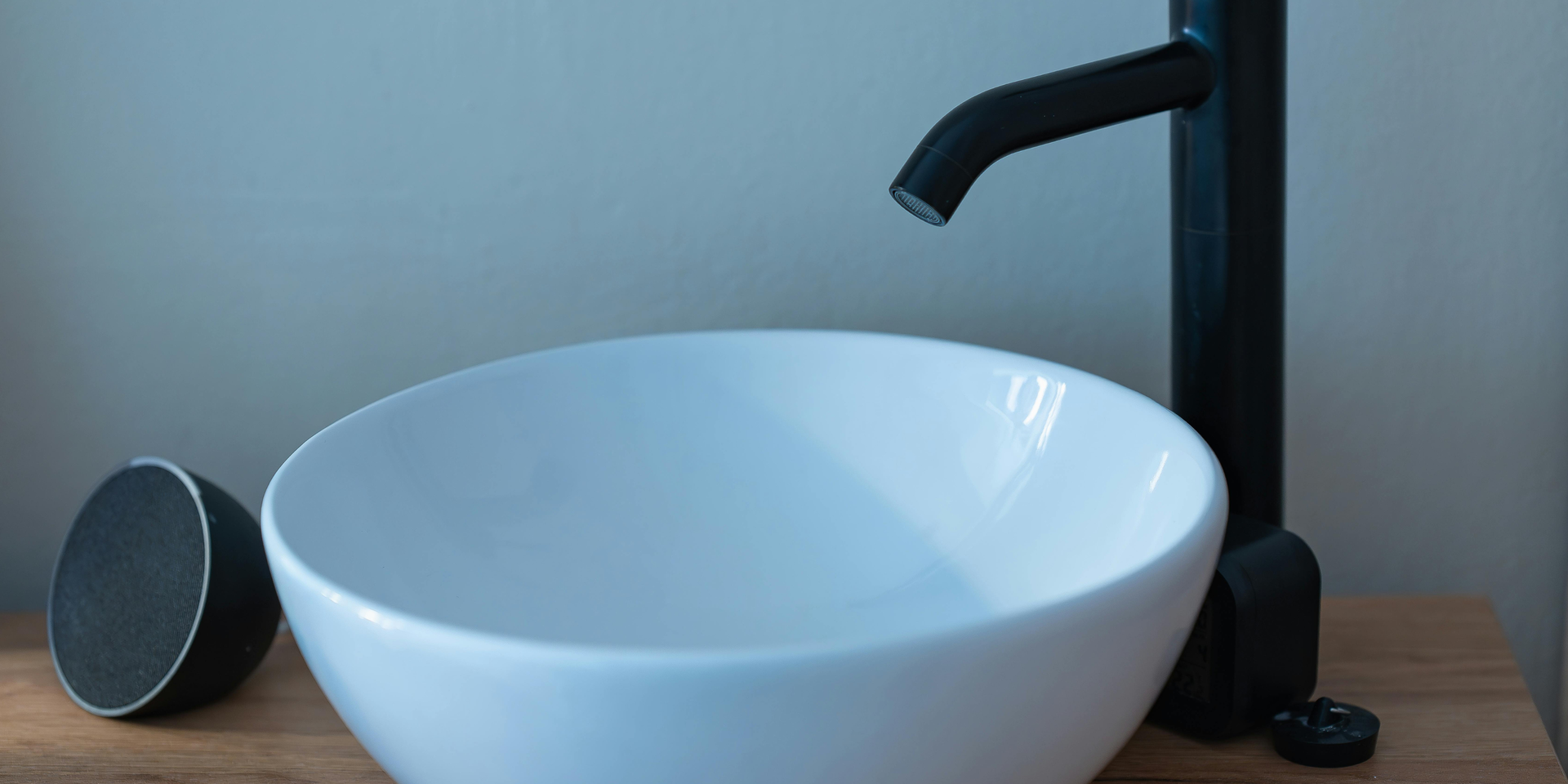 White bowl sink with black faucet, a small speaker sits to the left.
