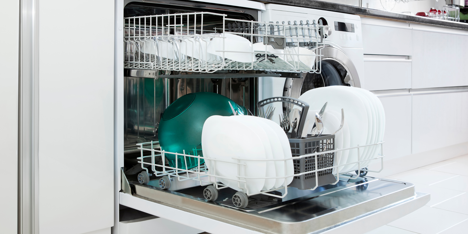 A dishwasher with open door, loaded with dishes of varying sizes and colors. White kitchen background.