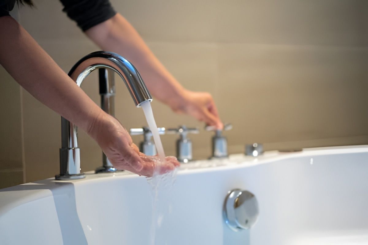 Person turning on faucet to fill a white bathtub. Water flows over their hand.