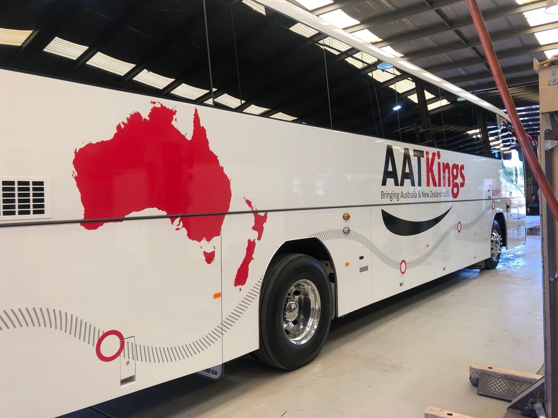 A White Bus With a Map of Australia on the Side is Parked in a Garage — Bluey's Signs in Ciccone, NT