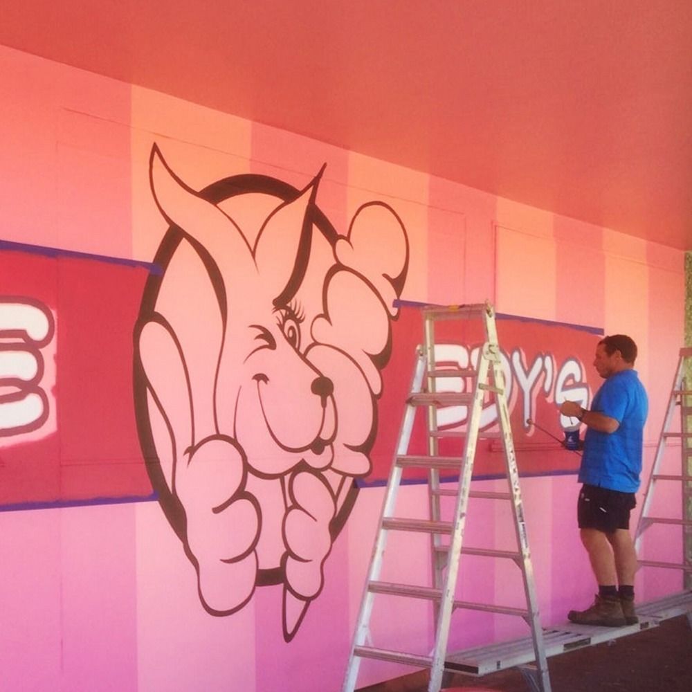 A Man on a Ladder is Painting a Bunny on a Pink Wall — Bluey's Signs in Ciccone, NT
