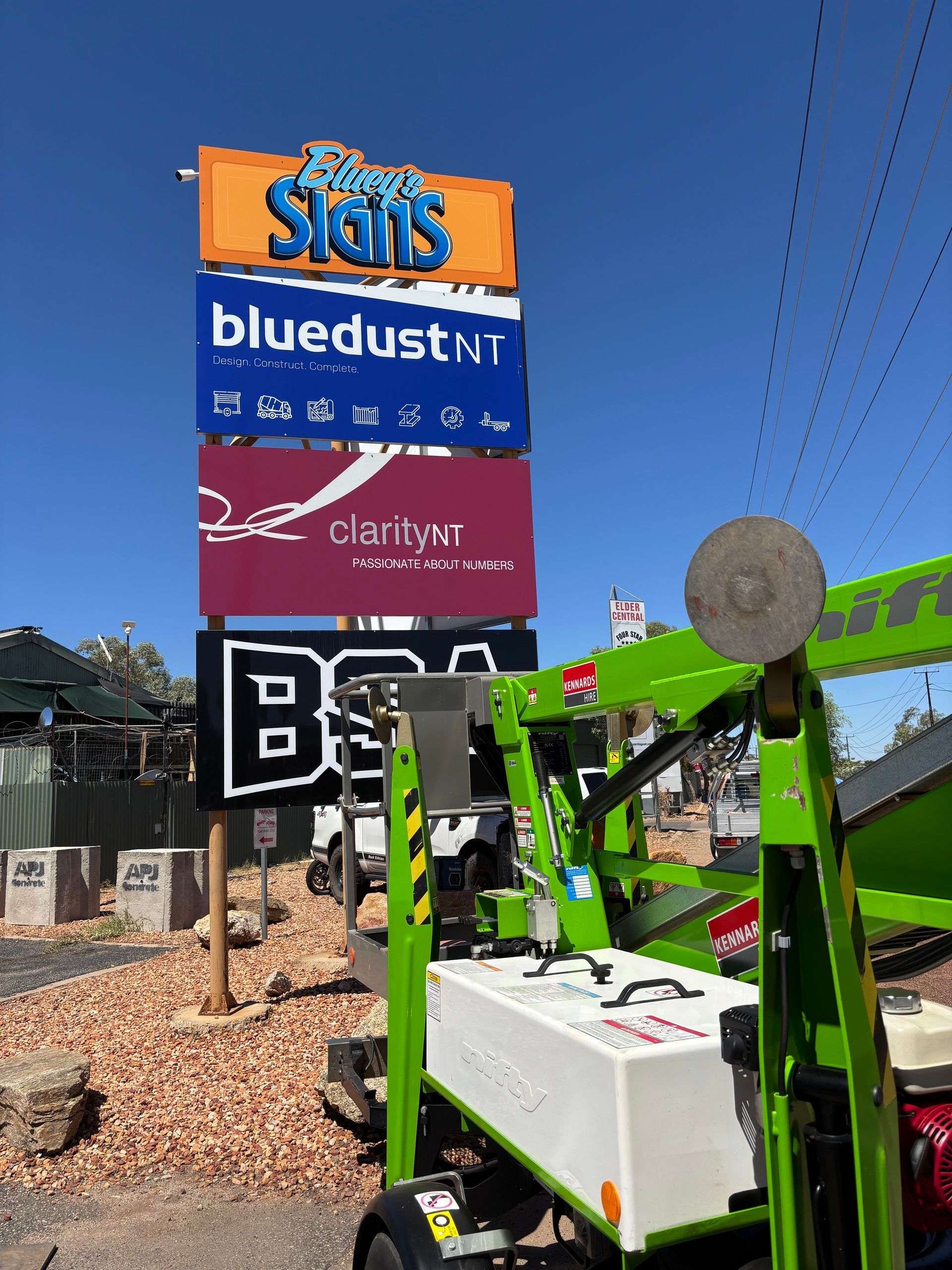 A Green Aerial Lift is Standing Next to a Sign That Says Bluedust — Bluey's Signs in Ciccone NT