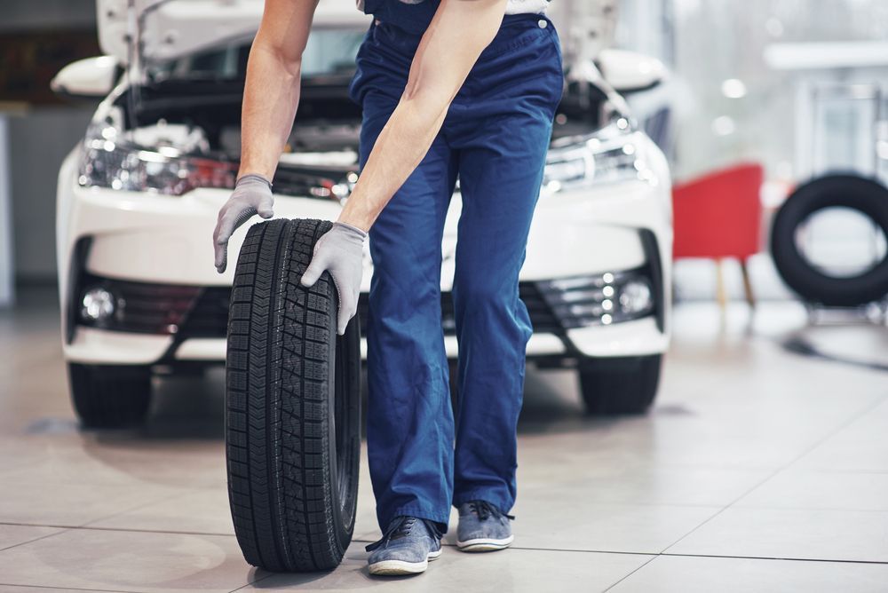 A man is holding a tire in front of a car in a garage | Autotek New South Wales