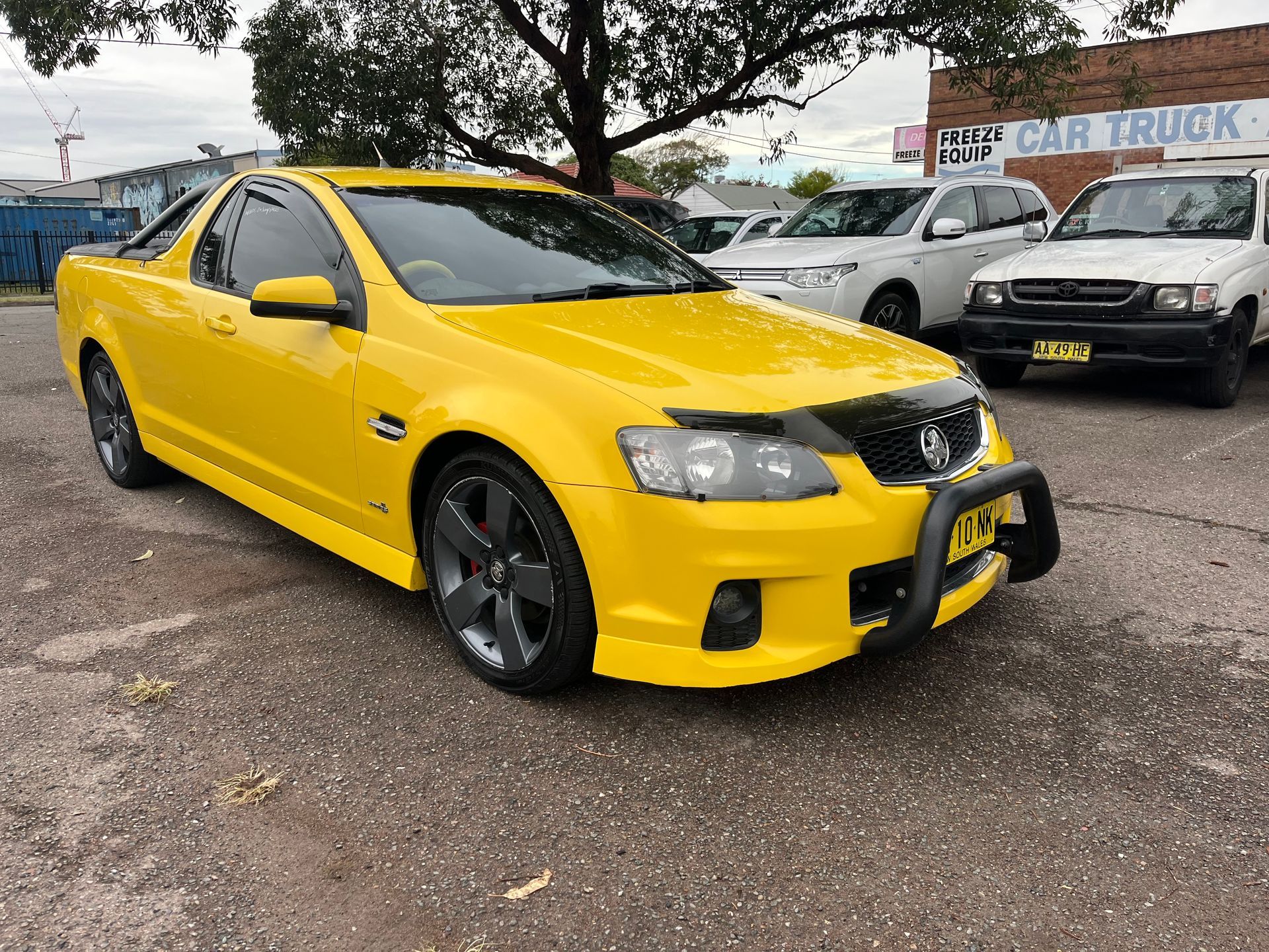 A yellow car is parked in a parking lot in front of a building | Autotek New South Wales