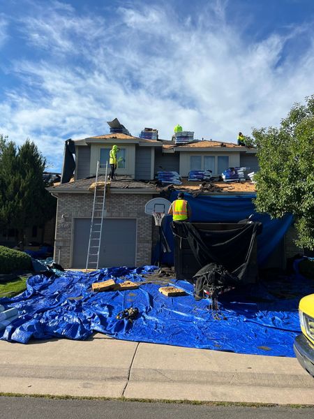 Roofers working on a house, surrounded by blue tarps, gray garage, bright sky.