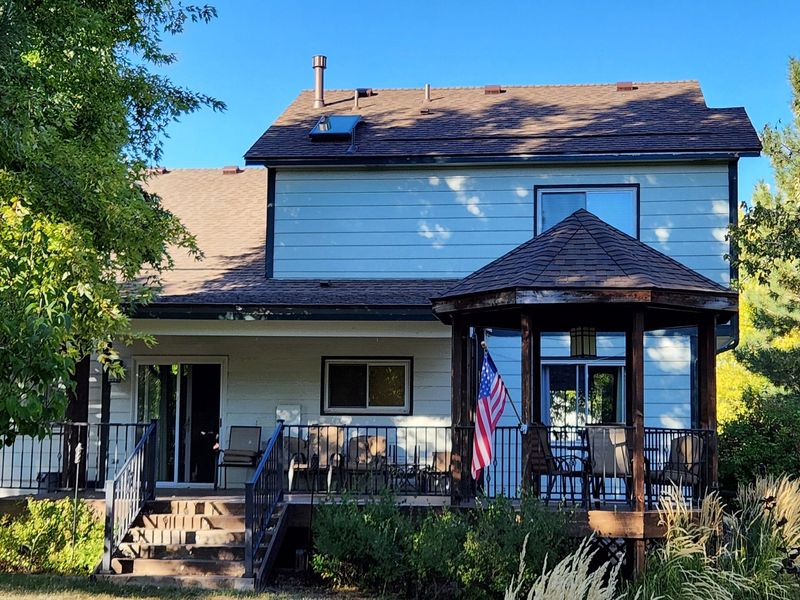 Two-story house with deck and gazebo. American flag. Green foliage frames the exterior.