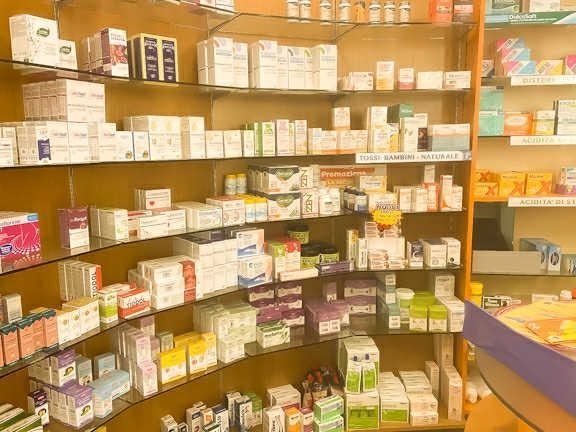 Scaffali pieni di medicinali e prodotti per la salute di vario genere nel corridoio di una farmacia.