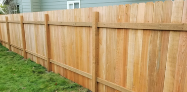 A wooden privacy fence made of vertical planks with horizontal support beams, standing in front of a house.