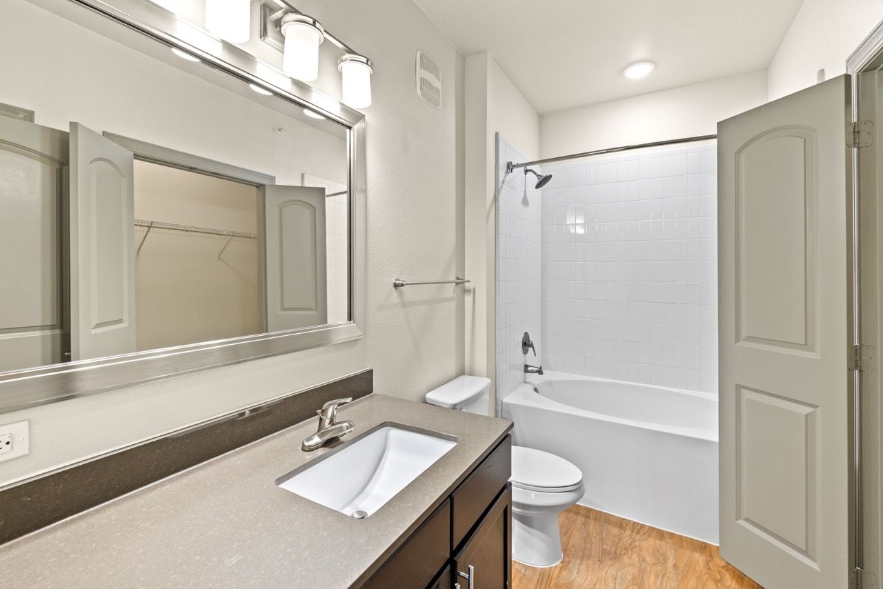 Apartment bathroom with vanity, mirror, toilet, and bathtub/shower.