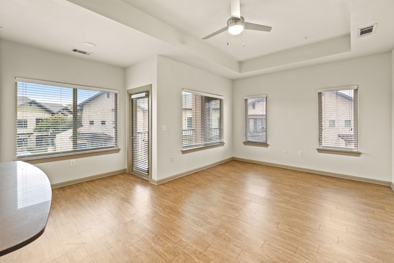 Bright living area with wood-look flooring, multiple windows with blinds, and a ceiling fan.