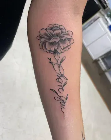 A woman has a tattoo of a carnation and the words `` i love you '' on her forearm.