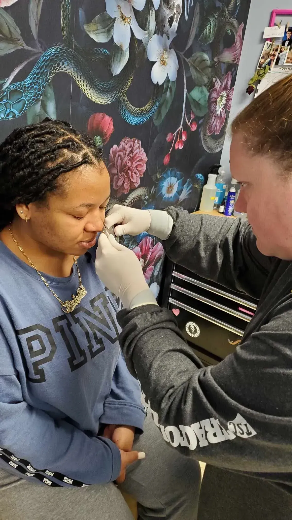 A woman is getting her nose pierced by a man in a pink shirt.
