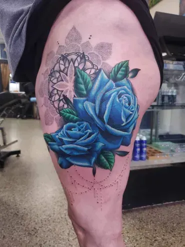 A person has a blue rose tattoo on their thigh.