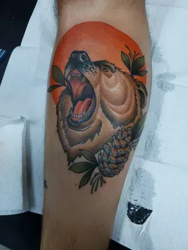 A person has a tattoo of a bear with a pine cone on their leg.