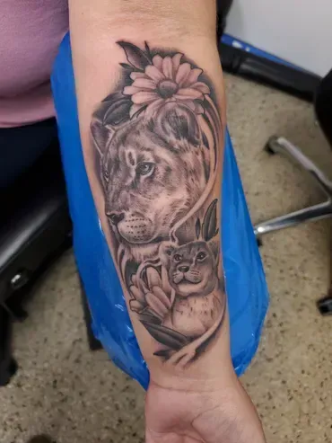 A woman has a tattoo of a lioness and her cub on her forearm.