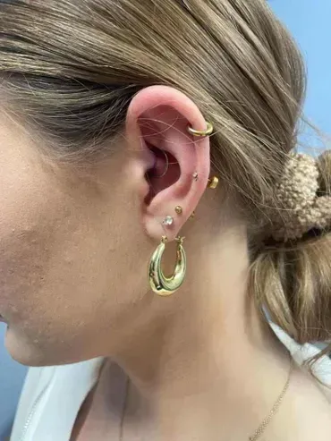 A close up of a woman 's ear with multiple piercings and hoop earrings.