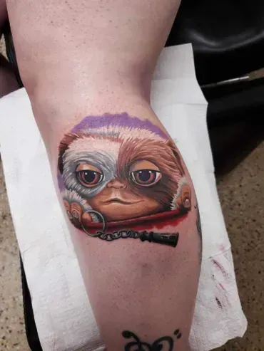 A person has a tattoo of a gremlin on their leg.