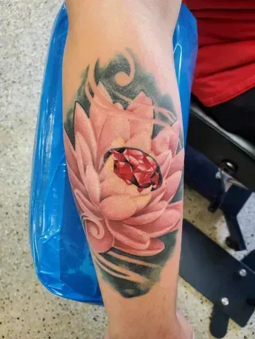 A person has a tattoo of a lotus flower with a ruby in it.